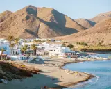 Pueblos de Almería con playa, casas blancas y palmeras junto a un mar azul, con montañas áridas de fondo.