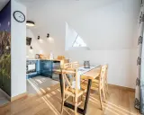 Przytulny apartament pod wierchem. W kuchni niebieskie szafki, jadalnia z drewnianym stołem. Na ścianie fototapeta z górami.