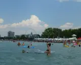 Tłum ludzi cieszy się słońcem i wodą na **Balaton plaża**. W tle widać diabelski młyn i budynki.