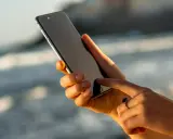 Dłoń trzyma iPhone 13, który nie chce się włączyć. Palec wskazujący próbuje go ożywić.