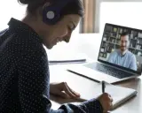Ragazza con cuffie sorride mentre prende appunti durante una lezione online, comprendendo il vero e-learning significato.