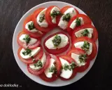 Pyszne pomidory z mozzarellą, ułożone na talerzu, ozdobione ziołami. Idealna przekąska na lato.