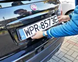 Mężczyzna montuje tablicę rejestracyjną. Pamiętaj o ważności dowodu rejestracyjnego, aby uniknąć problemów.