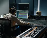 Ingénieur du son aux commandes d'une console, peut-être analogique ou numérique, dans un studio d'enregistrement.