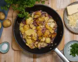 Bratkartoffeln rezept: goldbraune Kartoffeln mit Zwiebeln und Käse in der Pfanne, dazu frische Petersilie und Salz.