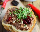 Pyszna pasta z czerwonej fasoli na chlebie, ozdobiona kiełkami i nasionami. Obok leżą czerwone papryczki chili.