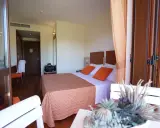 Camera accogliente al Valtur Otium Resort, con letto comodo, cuscini arancioni e vista sulla porta scorrevole in legno.