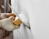 Manos enguantadas aplican yeso a una pared con una llana. La pregunta es: cuanto tarda en secar el yeso.