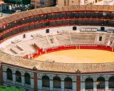 Leere Plaza de Toros mit roten Geländern und sandiger Arena. Die Sitzreihen sind leer, die Sonne scheint auf die traditionelle Architektur.