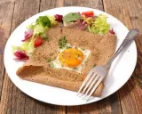 Galette bretonne complète au four, garnie d'un œuf au plat, d'herbes et servie avec une salade fraîche.