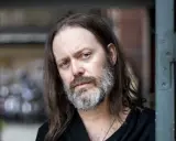 Niclas Frisk med långt hår och skägg, blickar mot kameran.