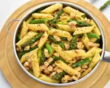 Penne z kurczakiem i szparagami, posypane płatkami chili. Pyszne danie na szybki obiad.