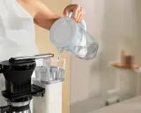 Eine Person füllt Wasser in eine Filterkaffeemaschine, um sie zu entkalken.