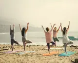 Kvinnor i trädposition på stranden. En lugn morgon för yoga, kanske en paus från pilates.