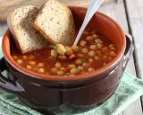 Una ciotola di terracotta con zuppa di ceci, pomodoro e rosmarino, accompagnata da fette di pane rustico.