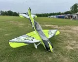 Ein ramy rc-Flugzeug mit auffälligem Design steht auf einer grünen Wiese. Im Hintergrund Zelte und Bäume.
