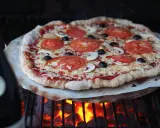 En hemmagjord pizza med tomater, champinjoner och oliver grillas över glödande kol. Perfekt för ett italiensk pizzadeg recept.