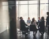 Grupa ludzi w garniturach podczas ważnego walnego zgromadzenia w sali konferencyjnej z widokiem na miasto.