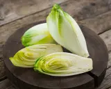 Frische Chicorée-Köpfe, einer davon halbiert, liegen auf einem Holzbrett. Perfekt für einen knackigen Chicorée-Salat.