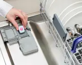 Dłoń wkłada tabletkę do zmywarki. Może to być rozwiązanie problemu, gdy zmywarka nie domywa górnego kosza.