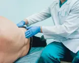 Lekarz od pęcherza w niebieskich rękawiczkach bada pacjenta leżącego na kozetce.