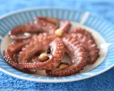 Gotowy ośmiornica przepis na talerzu z niebieskimi paskami. Delikatne macki z czosnkiem, idealne do degustacji.
