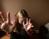 Dziewczyna z rozczochranymi włosami, z rękami przed twarzą, jakby broniła się przed nadmierną kontrolą.