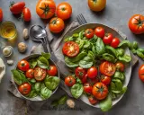 Deux salades de tomates fraîches et basilic, avec des tomates entières et coupées, sur fond gris.