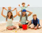 Famiglia felice in spiaggia, un modo perfetto per imparare come abbronzarsi in sicurezza mentre i bambini giocano con secchiello e palette.