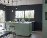 Cuisine moderne aux murs gris anthracite. L'îlot central vert sauge et le plan de travail en bois clair invitent à la convivialité. Quelle peinture pour plafond ? Un blanc mat pour agrandir l'espace.