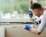 Mężczyzna w rękawiczkach nakłada piankę montażową na parapet. Czas, ile schnie pianka montażowa, zależy od warunków.