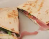Pyszna piadina z szynką, pomidorami i rukolą, złożona na pół, prezentuje apetyczny przekrój.