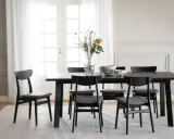 Svart matbord med sex stolar, en vas med blommor och en skål. Modern inredning matplats med ljus matta och vita dörrar i bakgrunden.