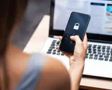Frau entsperrt Handy mit Schloss-Symbol, besorgt wegen gehackter mailadresse. Laptop im Hintergrund.