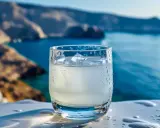 Szklanka orzeźwiającego ouzo z lodem na tle greckiego wybrzeża. Zastanawiasz się, ouzo ile ma procent? Zazwyczaj 40-50%.