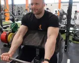 Mann trainiert Bizeps mit Langhantel im Fitnessstudio. Deutlich sichtbare Muskeln beim Bizeps dehnen.