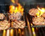 Flera saftiga hamburgare grillas över öppna lågor. Doften av sommar och grillning sprider sig.