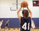 Ragazza con palla da basket, un ottimo sport per bambini iperattivi. In campo, altre giocatrici si preparano.