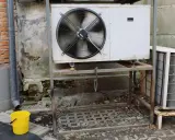 Unidad exterior de aire acondicionado goteando en invierno. Un cubo amarillo recoge el agua.