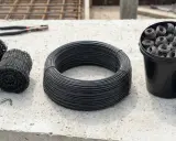Na betonie leżą zwoje drutu, wiązałka i szczypce. Materiały do wiązania zbrojenia.