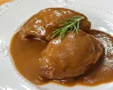 Deliciosas carrilleras de cerdo estofadas en salsa, coronadas con una ramita de romero fresco.