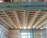 Widok od dołu na betonowe belki stropowe i pustaki ceramiczne, ukazujące różne rodzaje stropów w trakcie budowy.