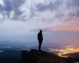 Silhouette di una persona su una rupe, con una città illuminata in lontananza. Un momento che fa amarcord, pensando a chi siamo e dove andiamo.