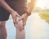 Mężczyzna trzyma się za kolano, odczuwając ból po rowerze. Słońce zachodzi na tle ścieżki.