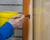 Persona aplica barniz a puerta de madera con brocha. Aprende como pintar puertas de madera para un acabado perfecto.