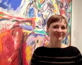 Kvinna ler framför en färgstark målning i Asger Jorns stil.