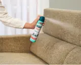 Mano rociando desinfectante en spray sobre un sillón de tela. Una forma fácil de saber como limpiar sillones de tela y eliminar olores.