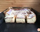 Pyszny sernik z mlekiem, pokrojony na kwadraty, polany białą polewą z czekoladowymi wzorami.