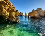 Felsformationen ragen aus dem klaren, türkisfarbenen Wasser. Der Levante-Wind kräuselt die Oberfläche und lässt die Sonne glitzern.
