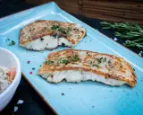 Zwei perfekt gegrillte Kabeljaufilets, mit Kräutern bestreut, serviert auf einem blauen Teller. Genießen Sie kabeljau grillen ohne alufolie!